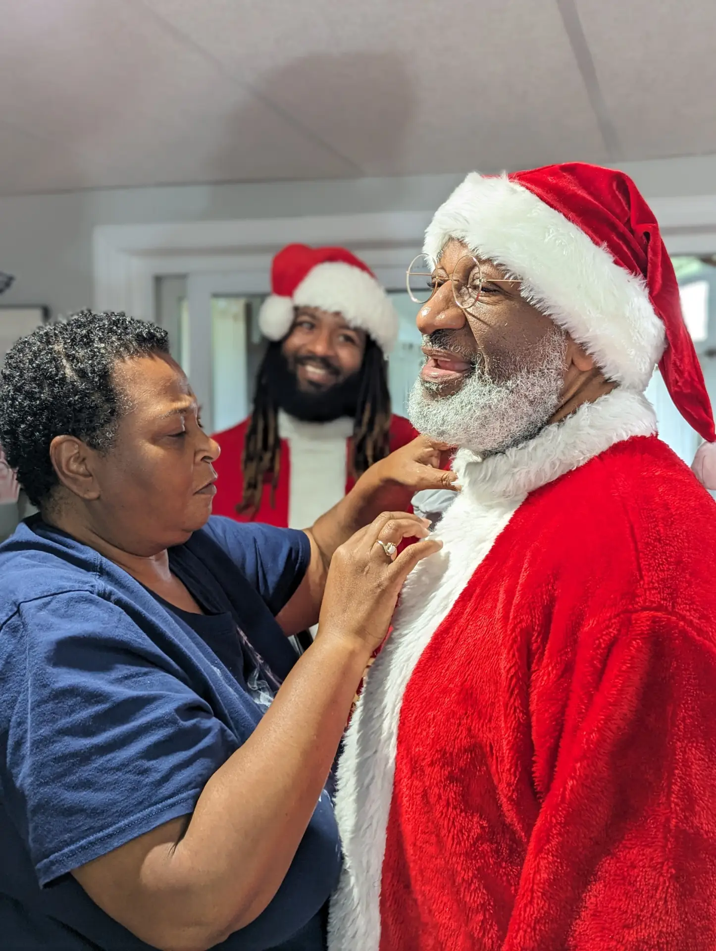 Crystal adjusting Santa Bruce's professional Black Santa suit, with Santa Chris smiling in the background.